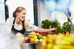 Smiling female looking away bowing over counter top to get fresh herbs.