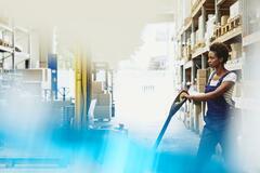 Female African-American worker operating a pallet loader in a logistics environment. Serious facial expression. Primary color blue. Secondary color white.