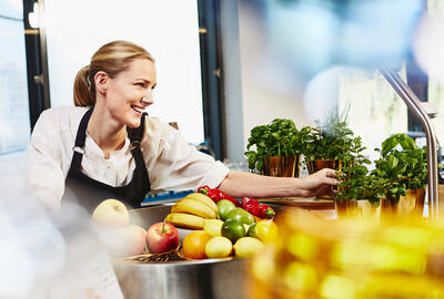 Smiling female looking away bowing over counter top to get fresh herbs.