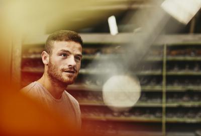 Blue-collar worker talking to someone. Looking up. Groomed beard. Caucasion man. Primary color yellow/orange.