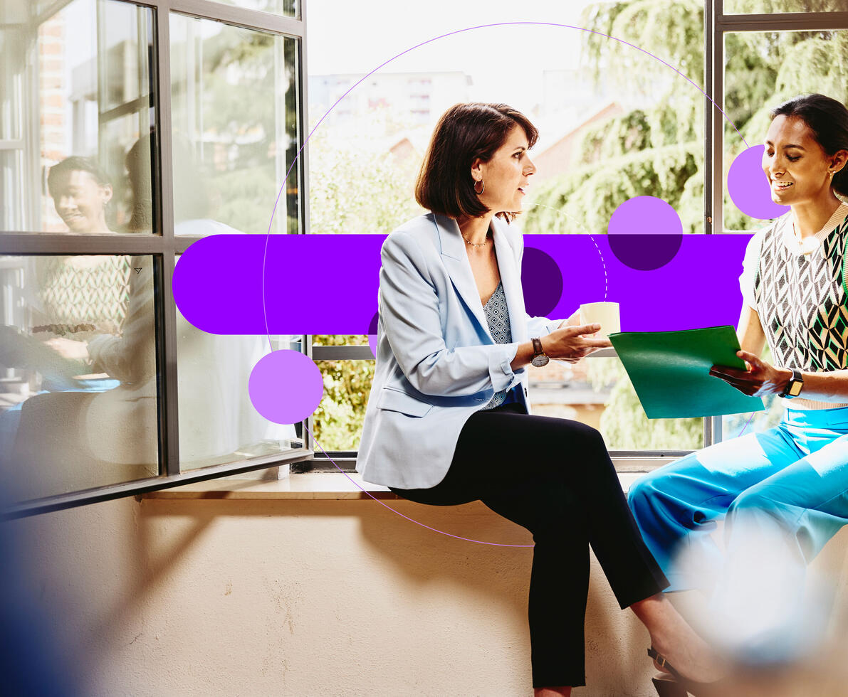 Two smiling females sitting by the window and discussing