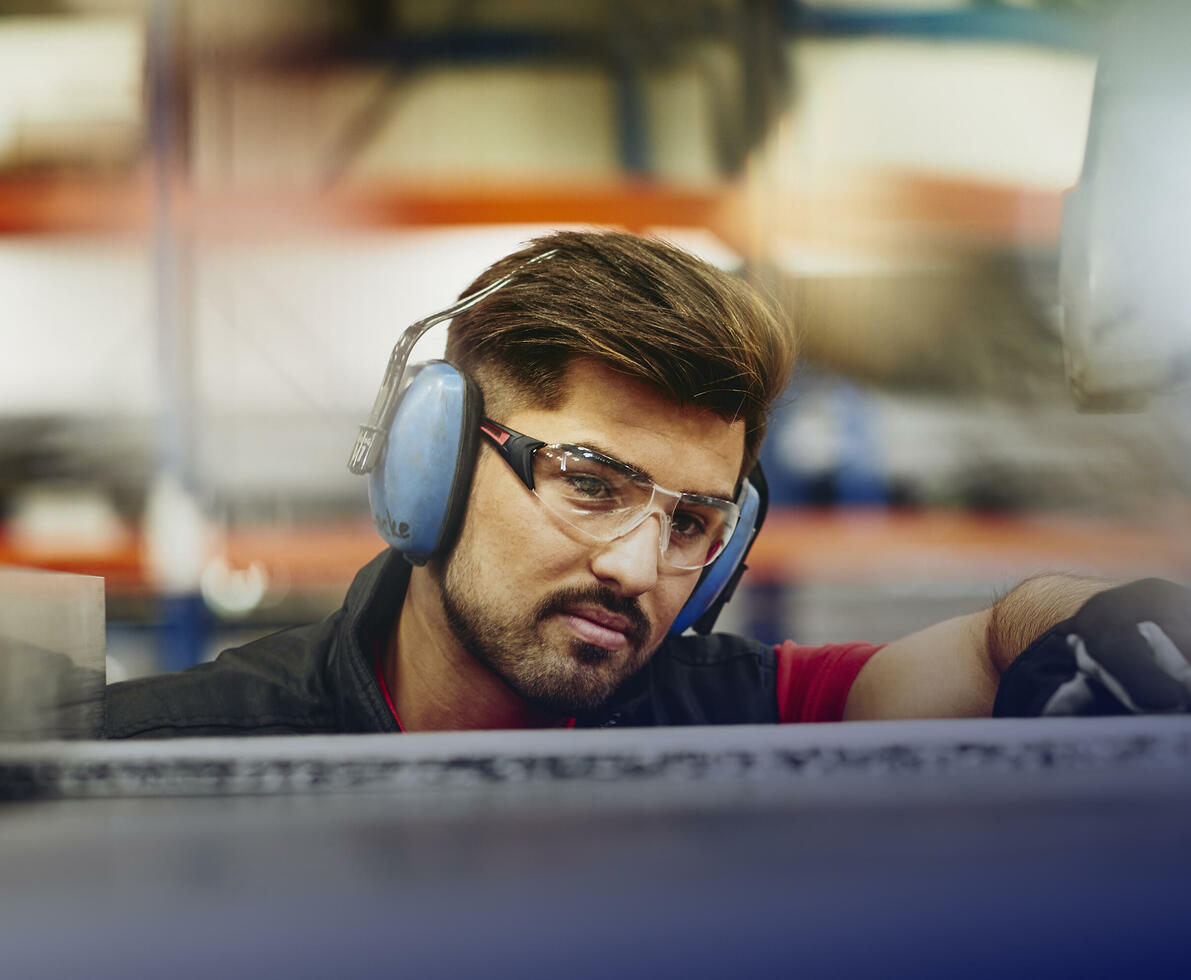 male wearing protective ear covers, safety gloves and safety glasses on a production site