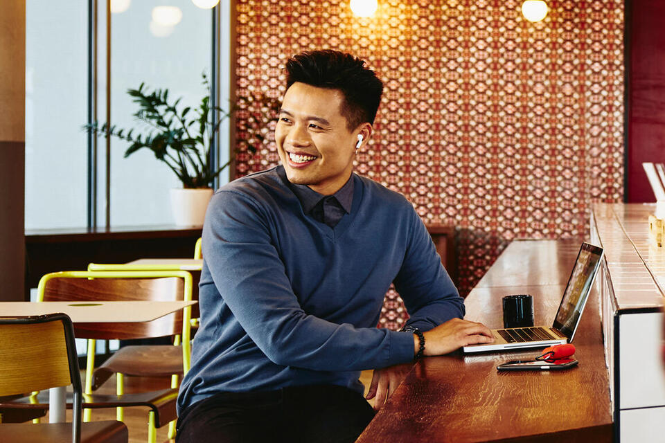 male looking away sitting in a restaurant smiling with laptop.