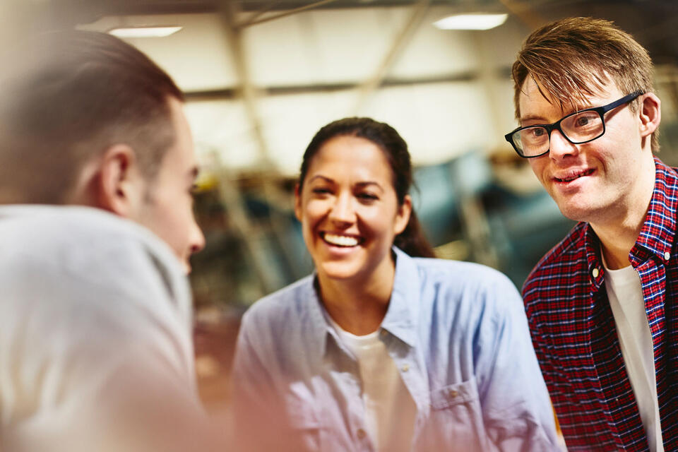 Three people having a conversation in a warehouse, smiling.